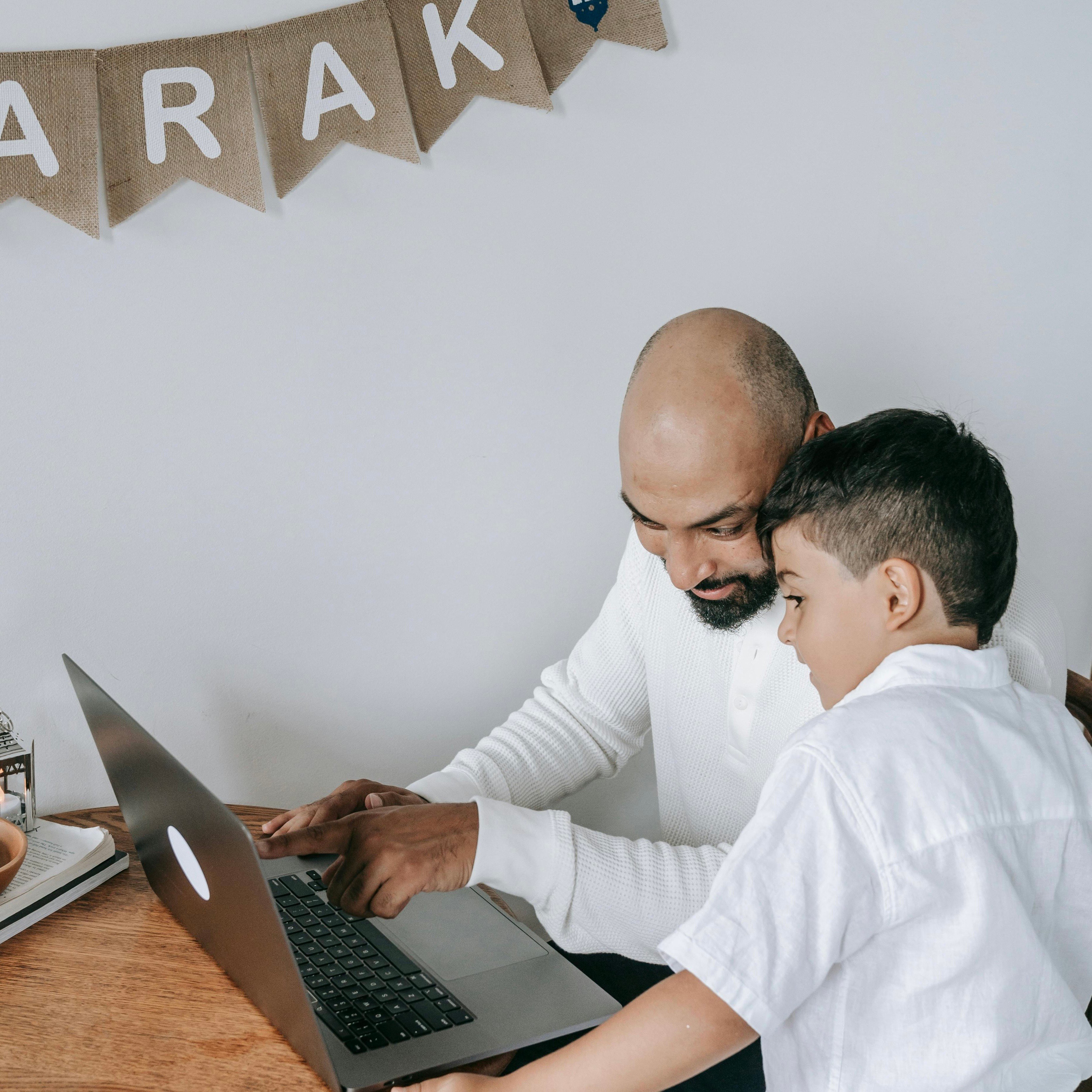 A Father and Son Look At A Laptop During The Month Of Ramadan