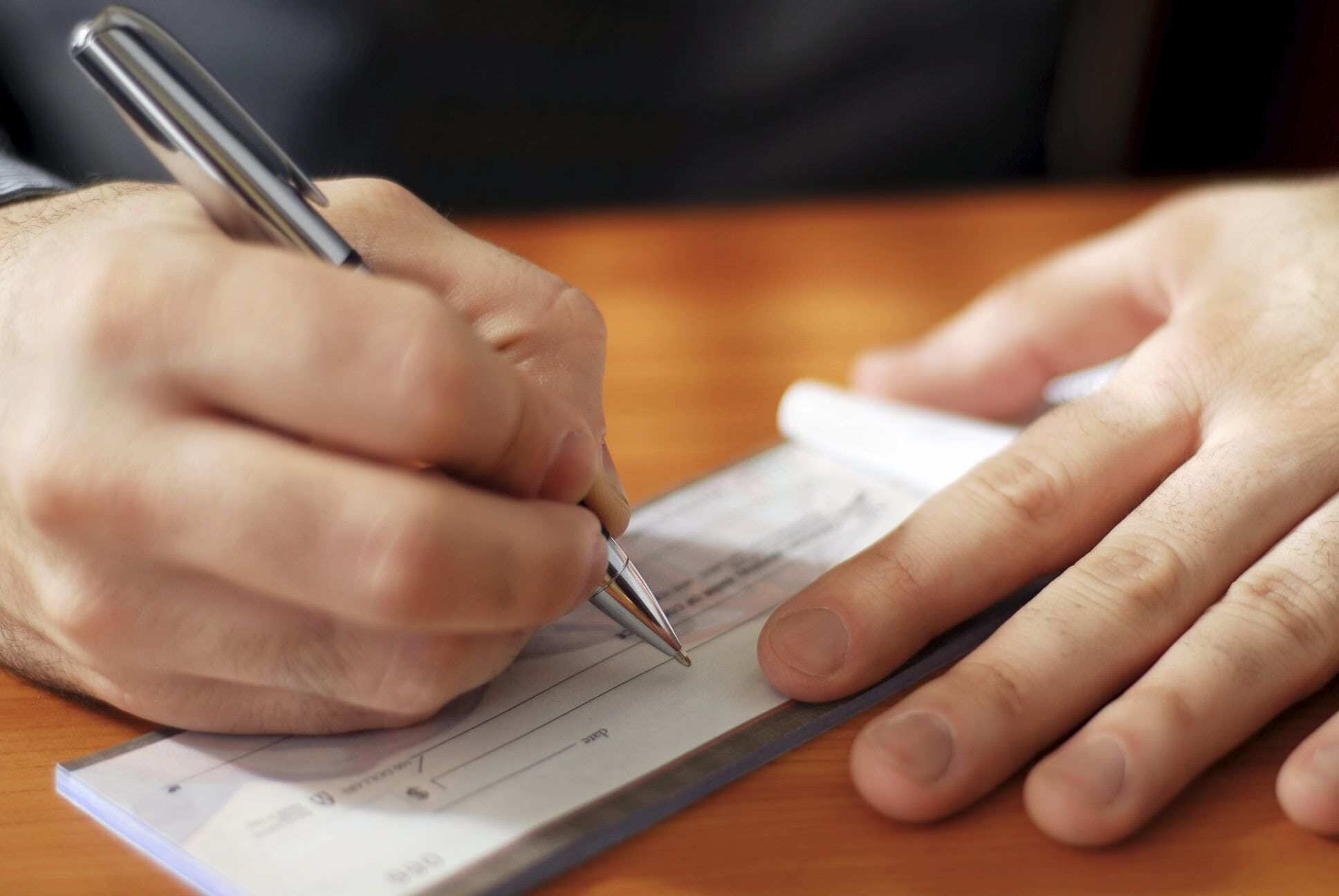 A white hand is holding a pen and signing a cheque